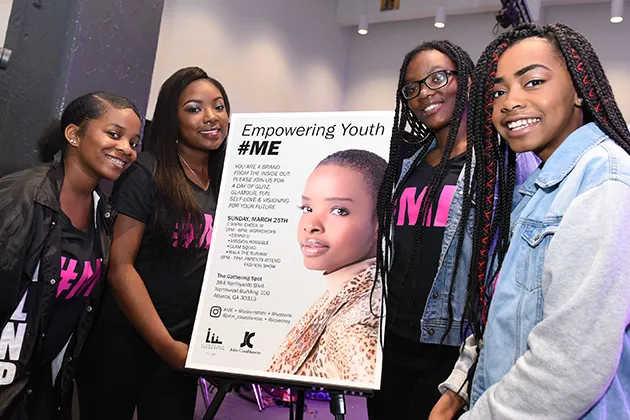 A group of young women stand with a sign that reads Empowering Youth #Me.